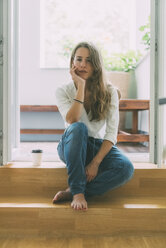 Young woman with takeaway coffee sitting at balcony - KNSF01632