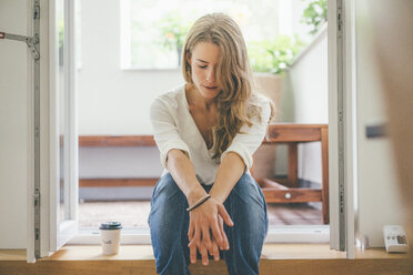 Junge Frau mit Kaffee zum Mitnehmen auf dem Balkon - KNSF01633