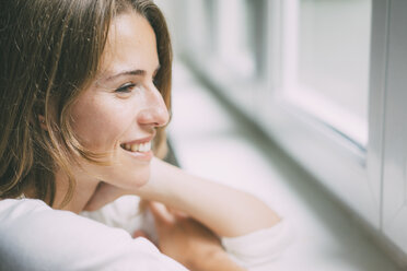 Smiling young woman looking out of the window - KNSF01640