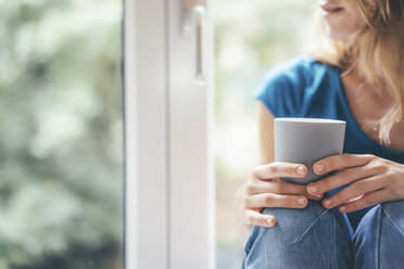 Nahaufnahme einer Frau, die ein Mobiltelefon am Fenster hält - KNSF01642