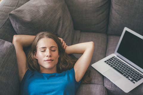 Junge Frau mit Laptop zu Hause auf der Couch liegend, lizenzfreies Stockfoto