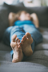 Feet of relaxed young woman lying on couch at home - KNSF01651