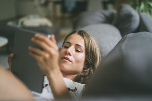 Entspannte junge Frau auf der Couch liegend mit Tablet - KNSF01654