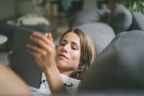 Relaxed young woman lying on couch using tablet - KNSF01654