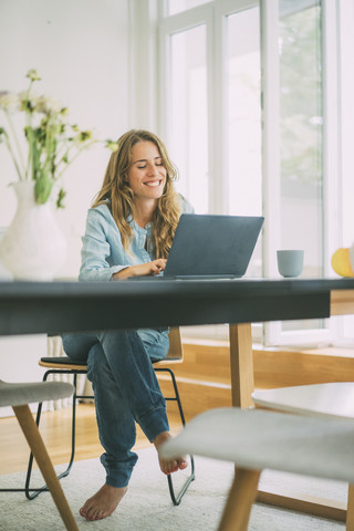 Lächelnde junge Frau, die zu Hause einen Laptop benutzt, lizenzfreies Stockfoto