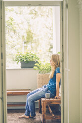 Entspannte junge Frau mit Tasse auf dem Balkon sitzend - KNSF01675