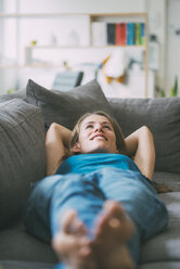 Smiling young woman lying on couch at home - KNSF01678