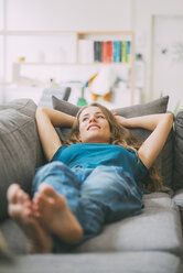Smiling young woman lying on couch at home - KNSF01679
