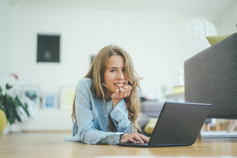 Porträt einer jungen Frau, die auf dem Boden liegt und einen Laptop benutzt, lizenzfreies Stockfoto