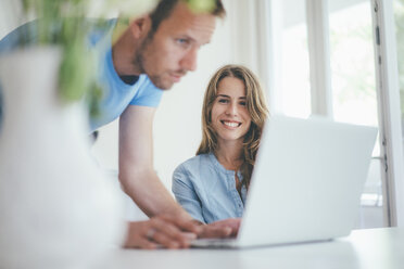 Lächelnde junge Frau und Mann verwenden Laptop zu Hause - KNSF01695