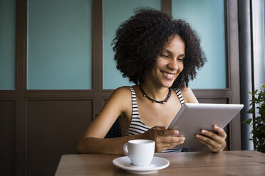 Junge Frau sitzt in einem Café und schaut auf ein Tablet - ABZF02141