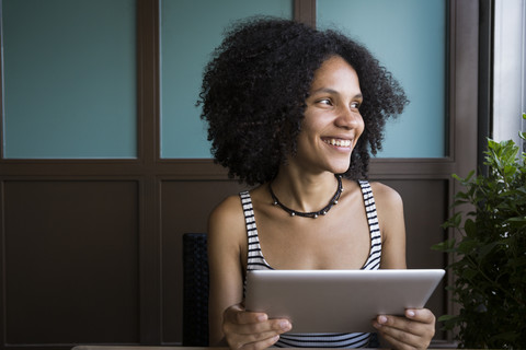 Lächelnde junge Frau mit Tablet in einem Café sitzend, lizenzfreies Stockfoto
