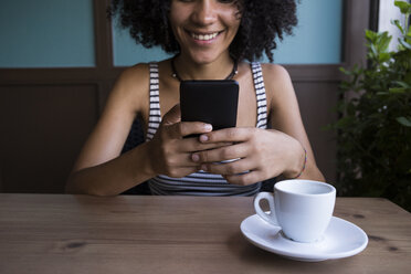 Young woman sitting in a coffee shop looking at smartphone - ABZF02144