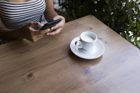 Junge Frau sitzt in einem Café und benutzt ein Mobiltelefon, Teilansicht, lizenzfreies Stockfoto