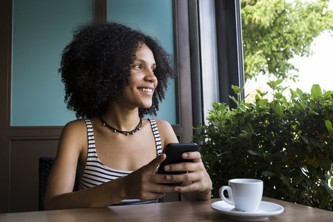 Young woman with smartphone sitting in a coffee shop looking out of window stock photo