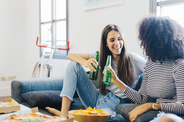 Friends clinking beer bottles sitting on the sofa - GIOF02802