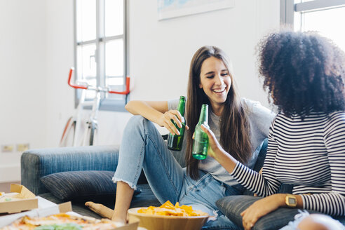 Freunde, die auf dem Sofa sitzend Bierflaschen anstoßen - GIOF02802