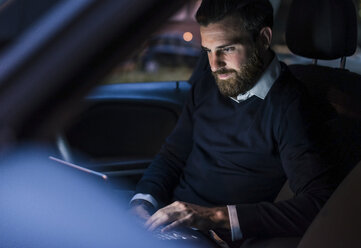 Geschäftsmann benutzt Laptop im Auto bei Nacht - UUF10877