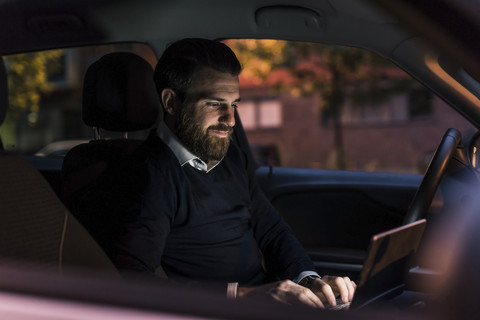 Geschäftsmann benutzt Laptop im Auto bei Nacht, lizenzfreies Stockfoto