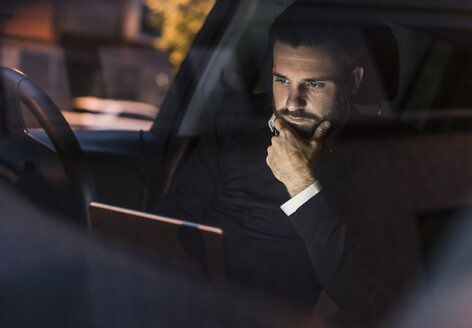 Businessman with laptop in car at night - UUF10879