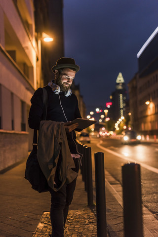 Stylish young man with tablet on urban street at night stock photo