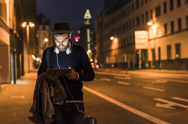 Stilvoller junger Mann mit Tablet auf einer nächtlichen Straße in der Stadt - UUF10885