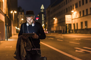 Stylish young man with tablet on urban street at night - UUF10885