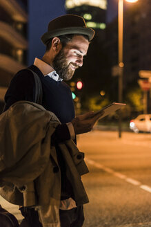 Stilvoller junger Mann mit Tablet auf einer nächtlichen Straße in der Stadt - UUF10886