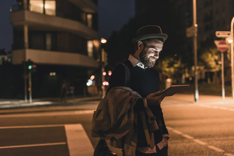 Stilvoller junger Mann mit Tablet auf einer nächtlichen Straße in der Stadt, lizenzfreies Stockfoto