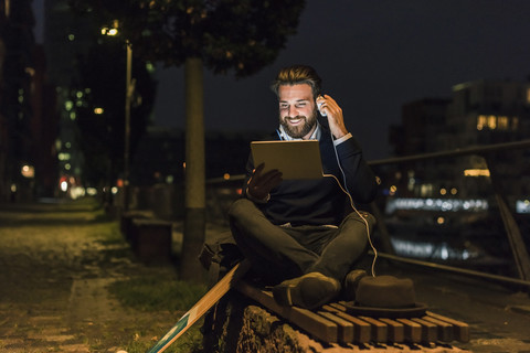 Lächelnder junger Mann mit Tablet und Kopfhörer in der Stadt bei Nacht, lizenzfreies Stockfoto