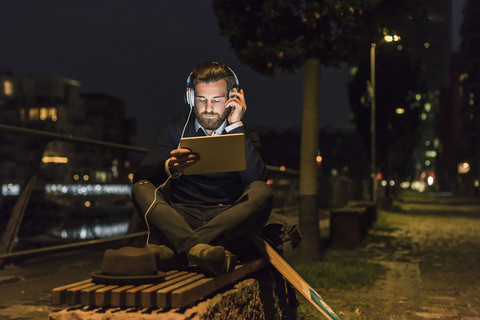 Young man with tablet and headphones in the city at night stock photo