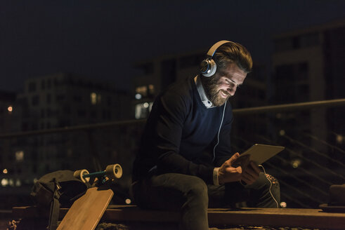 Smiling young man with tablet and headphones in the city at night - UUF10892