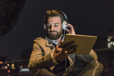 Junger Mann mit Tablet und Kopfhörer in der Stadt bei Nacht, lizenzfreies Stockfoto