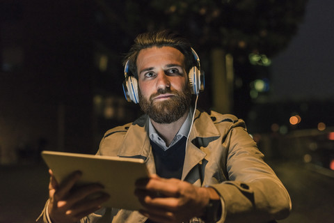 Junger Mann mit Tablet und Kopfhörer in der Stadt bei Nacht, lizenzfreies Stockfoto