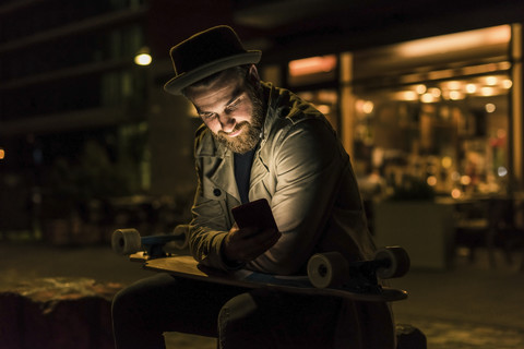 Stilvoller junger Mann mit Mobiltelefon in der Stadt bei Nacht, lizenzfreies Stockfoto