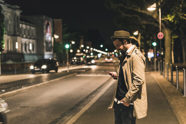 Stilvoller junger Mann mit Handy auf einer nächtlichen Straße in der Stadt - UUF10900