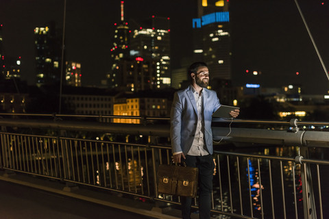 Junger Mann mit Tablet und Kopfhörer auf städtischer Brücke bei Nacht, lizenzfreies Stockfoto