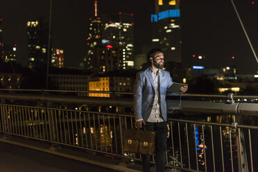 Junger Mann mit Tablet und Kopfhörer auf städtischer Brücke bei Nacht - UUF10902
