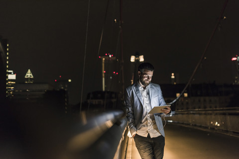 Young man with tablet and earphone on urban bridge at night stock photo