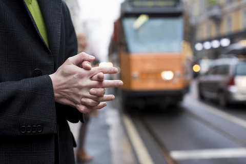 Nahaufnahme eines Geschäftsmannes mit gefalteten Händen in der Stadt an einer Straßenbahnhaltestelle, lizenzfreies Stockfoto
