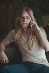 Portrait of young man with long hair and beard using smartphone at home - RTBF00957