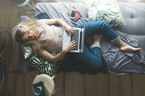 Schlafender junger Mann mit Laptop und Kopfhörern auf dem Schlafsofa, lizenzfreies Stockfoto