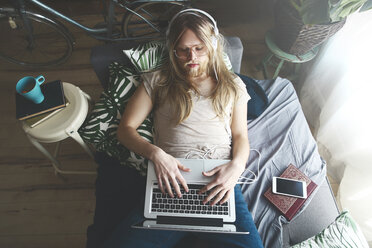 Man with long hair and beard using laptop on sofa bed - RTBF00963