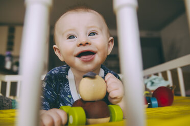 Porträt eines glücklichen kleinen Jungen mit Holzspielzeug in seinem Kinderbett - MFF03675