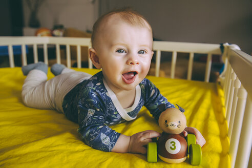 Porträt eines kleinen Jungen mit Holzspielzeug in seinem Kinderbettchen - MFF03676