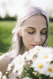 Frau mit geschlossenen Augen hält einen Strauß Gänseblümchen - GIOF02823