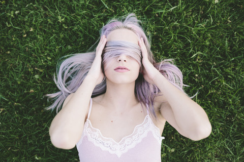 Frau liegt im Gras und bedeckt die Augen mit ihren Haaren, lizenzfreies Stockfoto