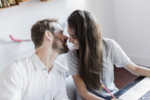 Glückliches Paar mit Laptop zu Hause küssend - GIOF02847