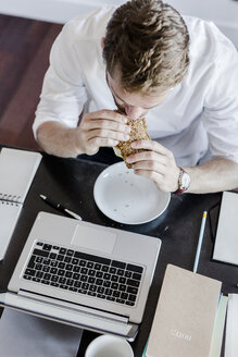 Mann mit Laptop beim Essen zu Hause - GIOF02854