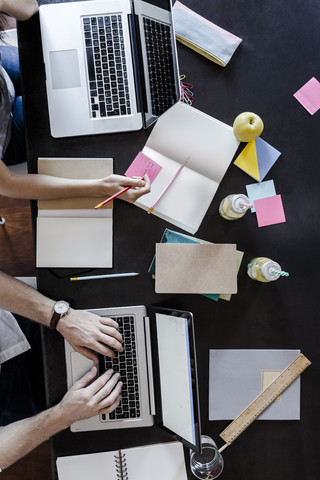 Draufsicht auf einen Mann und eine Frau, die Laptops benutzen und Notizen machen, lizenzfreies Stockfoto